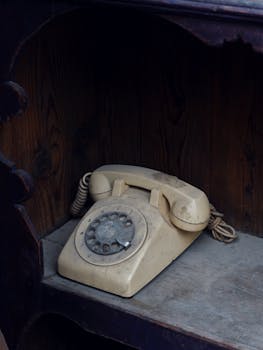 Classic beige rotary dial telephone on a dusty wooden shelf, evoking nostalgia and retro charm.
