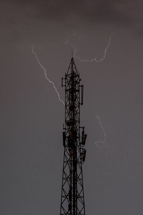 Free A dramatic image of lightning striking behind a broadcast tower during a thunderstorm. Stock Photo