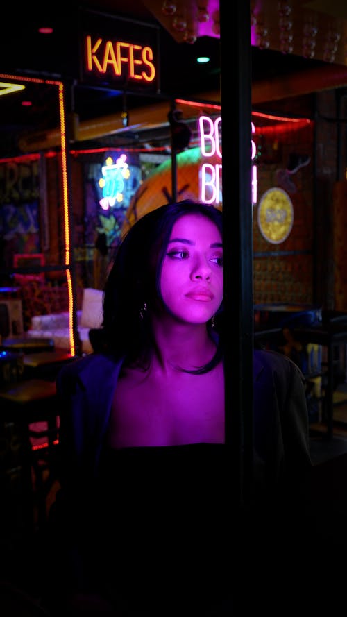 Woman behind Window of Bar Decorated with Neon Signs