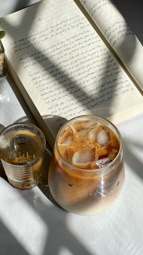 Free A refreshing iced coffee beside an open book, bathed in natural sunlight, casting intriguing shadows. Stock Photo