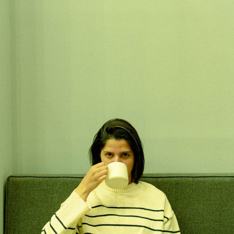 Young Woman Sitting On Couch Drinking From Mug