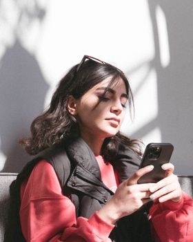 Side profile of a woman using her smartphone indoors with natural sunlight shadows on a white background.