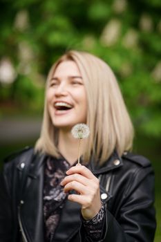 A joyful woman holding a dandelion, laughing in a spring garden.