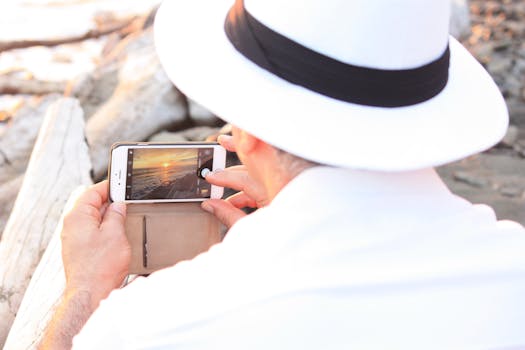 一名男子戴着白帽子，用智能手机拍摄了宁静的海滩日落