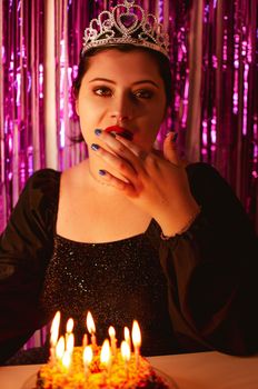 Woman celebrates birthday in style with a sparkling crown and lit candles creating a festive mood.