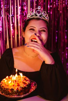 Smiling woman wearing a tiara enjoying her birthday with a lit cake.