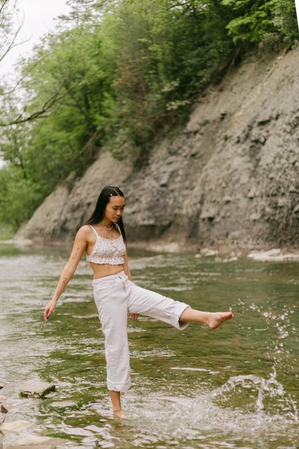 Carefree young woman playing by the river edge in casual fashion, enjoying nature.