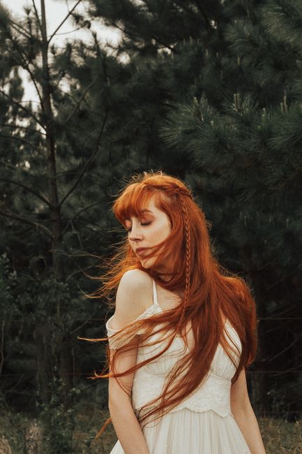 Beautiful redhead woman posing peacefully in a lush green forest, exuding tranquility and natural elegance.