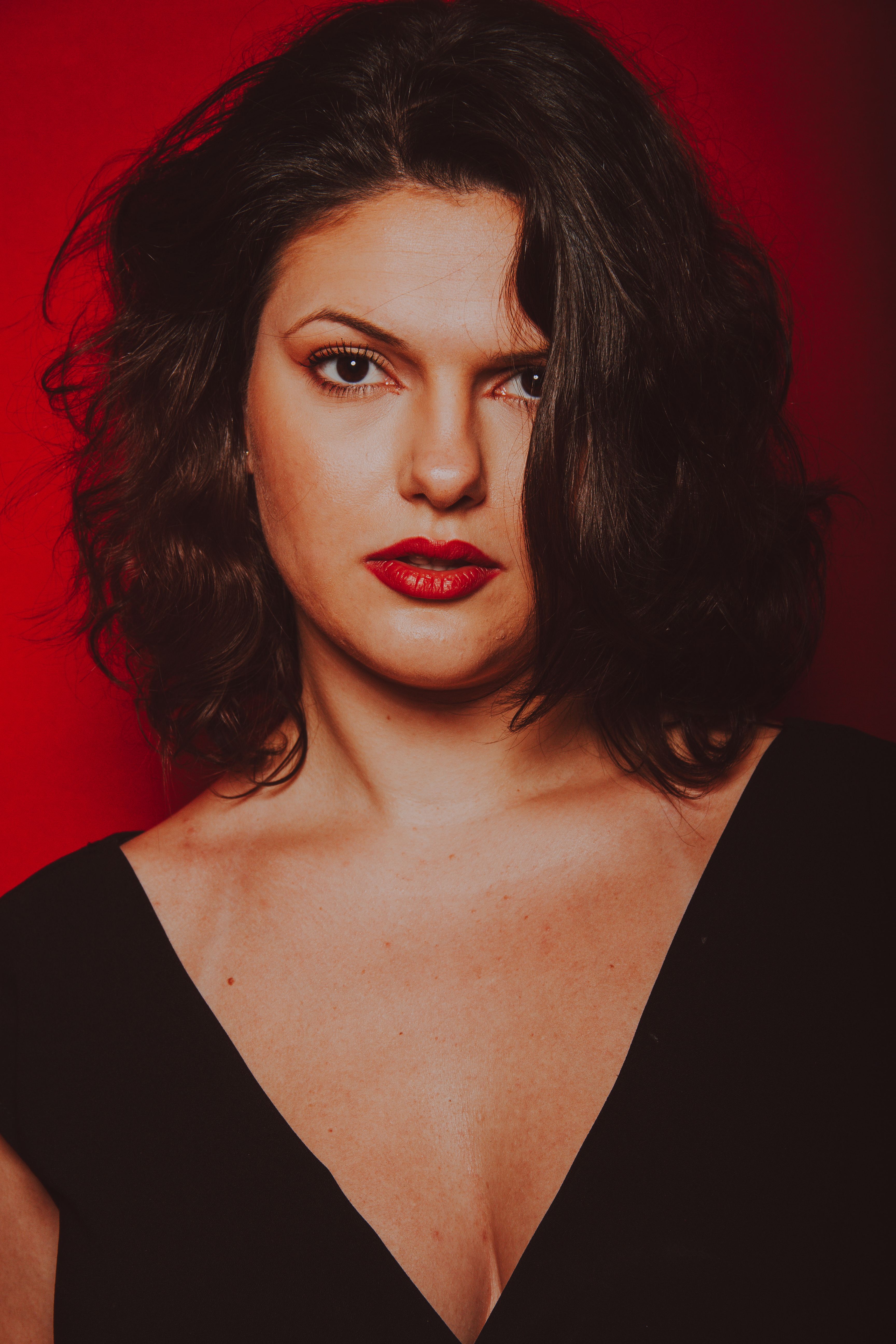 A glamorous portrait of a young woman with makeup, set against a vibrant red studio background.