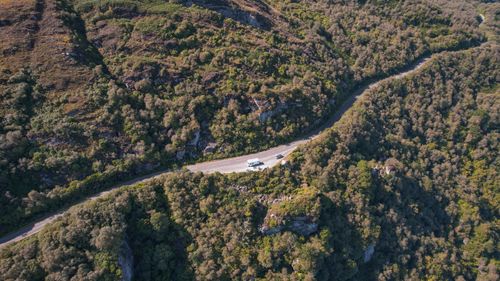 Free Aerial view of a winding road through lush forest and hills in Tighnabruaich, Scotland. Stock Photo