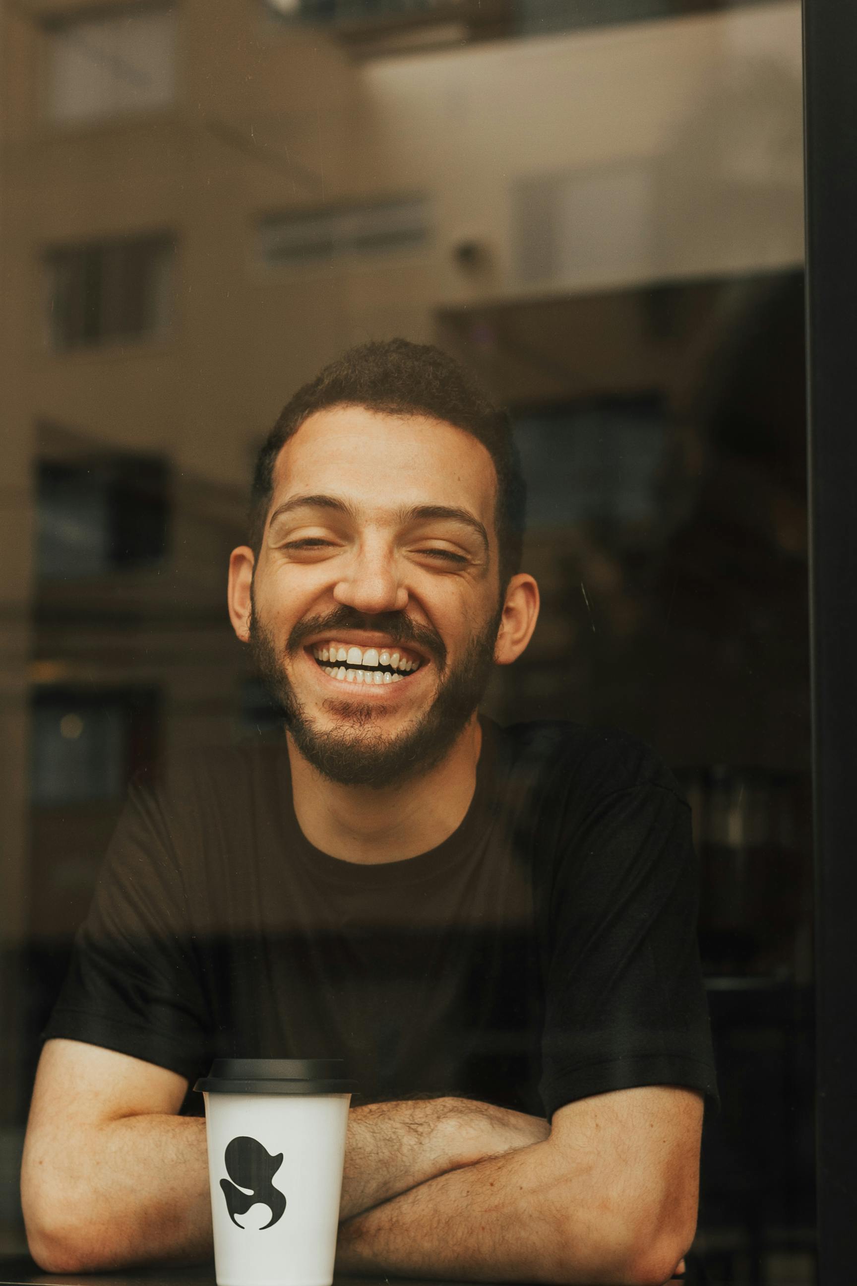 Smiling bearded man with takeaway cup in cafe window free stock photo
