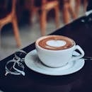 一张心形泡沫的卡布奇诺照片，桌上还放着一副眼镜