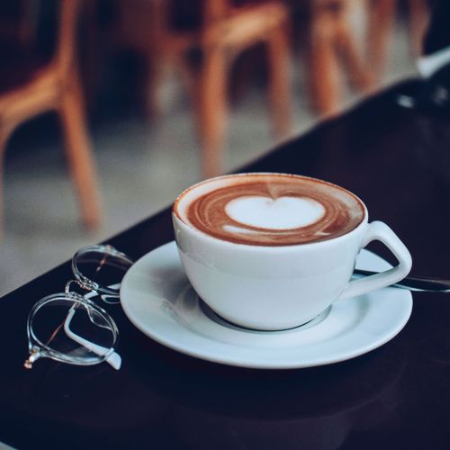 Free Aesthetic photo of a cappuccino with heart foam, accompanied by eyeglasses on a table. Stock Photo