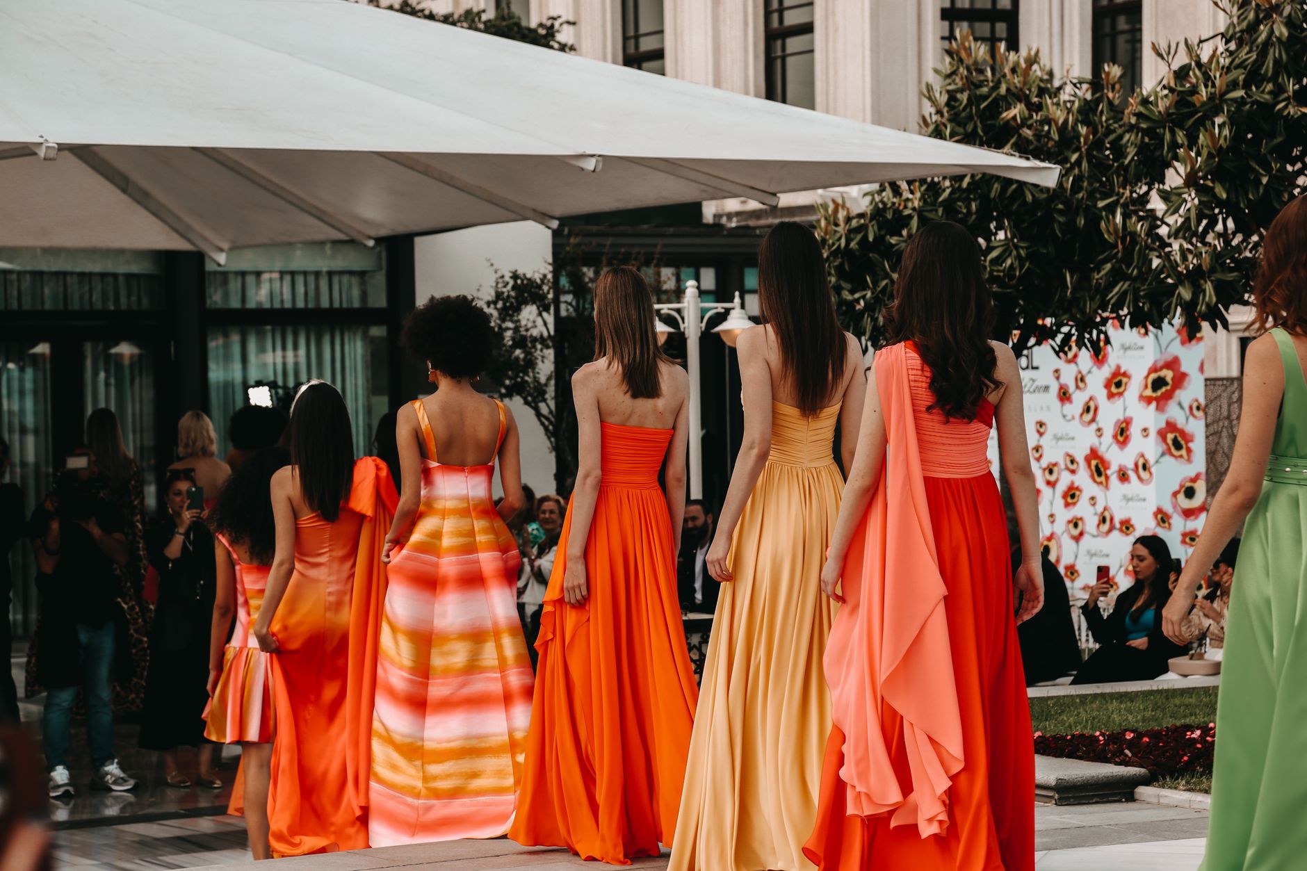 Models in stunning vibrant dresses walk the runway in an outdoor fashion show.