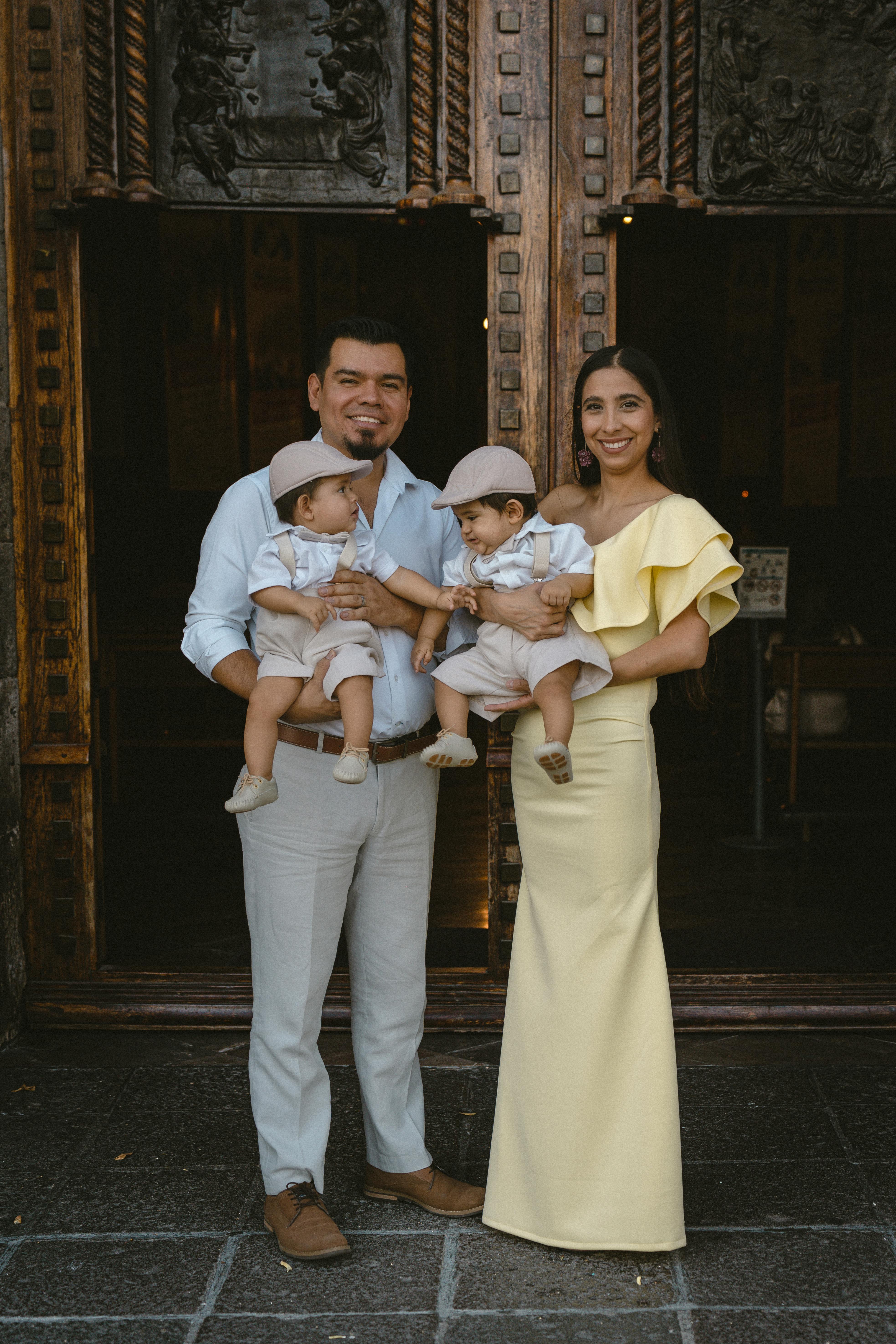 Happy family with twin boys posing at a church entrance dressed in formal attire.