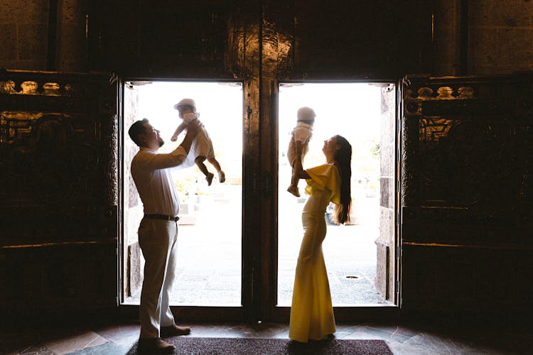 Couple Standing In Open Church Doors Holding Their Babies