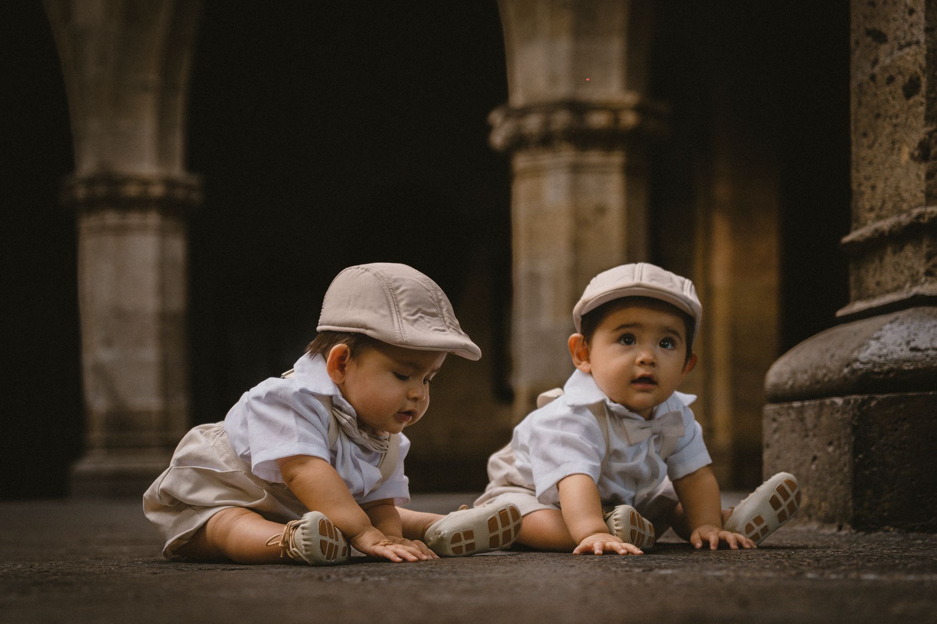 Charming twin babies in matching outfits exploring a historic courtyard with a curious gaze.