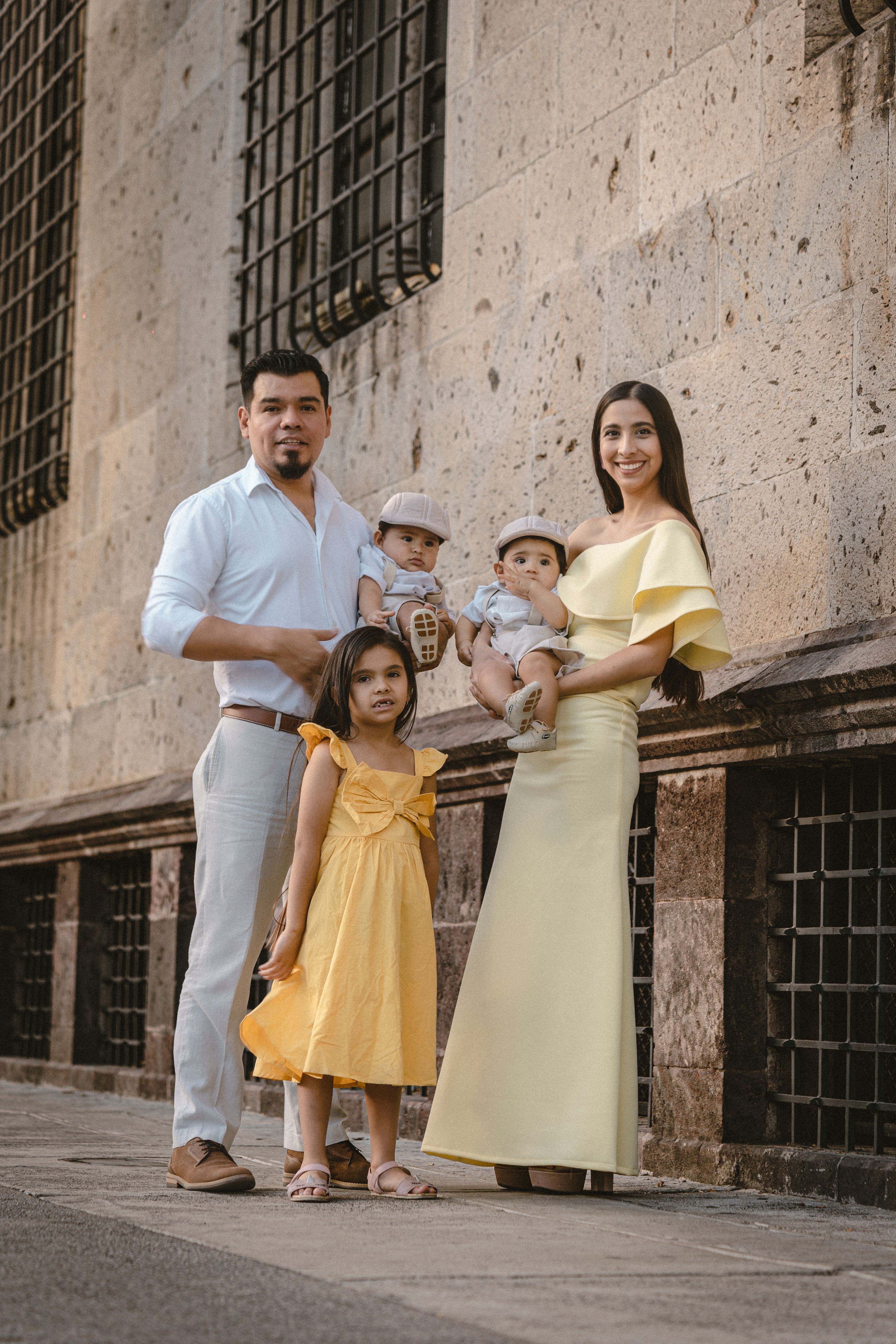 Charming family portrait in urban setting with historic stone wall. Mother, father, and kids smiling.