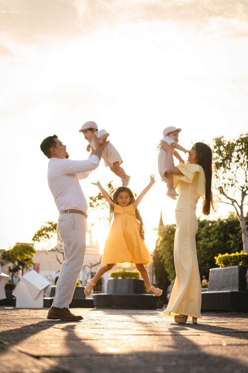 Free Happy family of four enjoying a playful moment in a sunlit park setting. Stock Photo