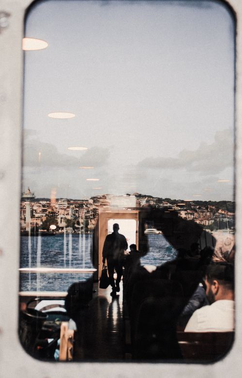 Free A reflective view of Istanbul through a ferry window with people onboard, capturing urban life and travel. Stock Photo