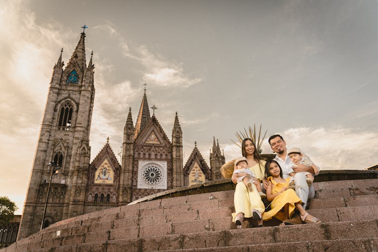 A Family With Three Kids Sitting On Steps In Front Of A Church 