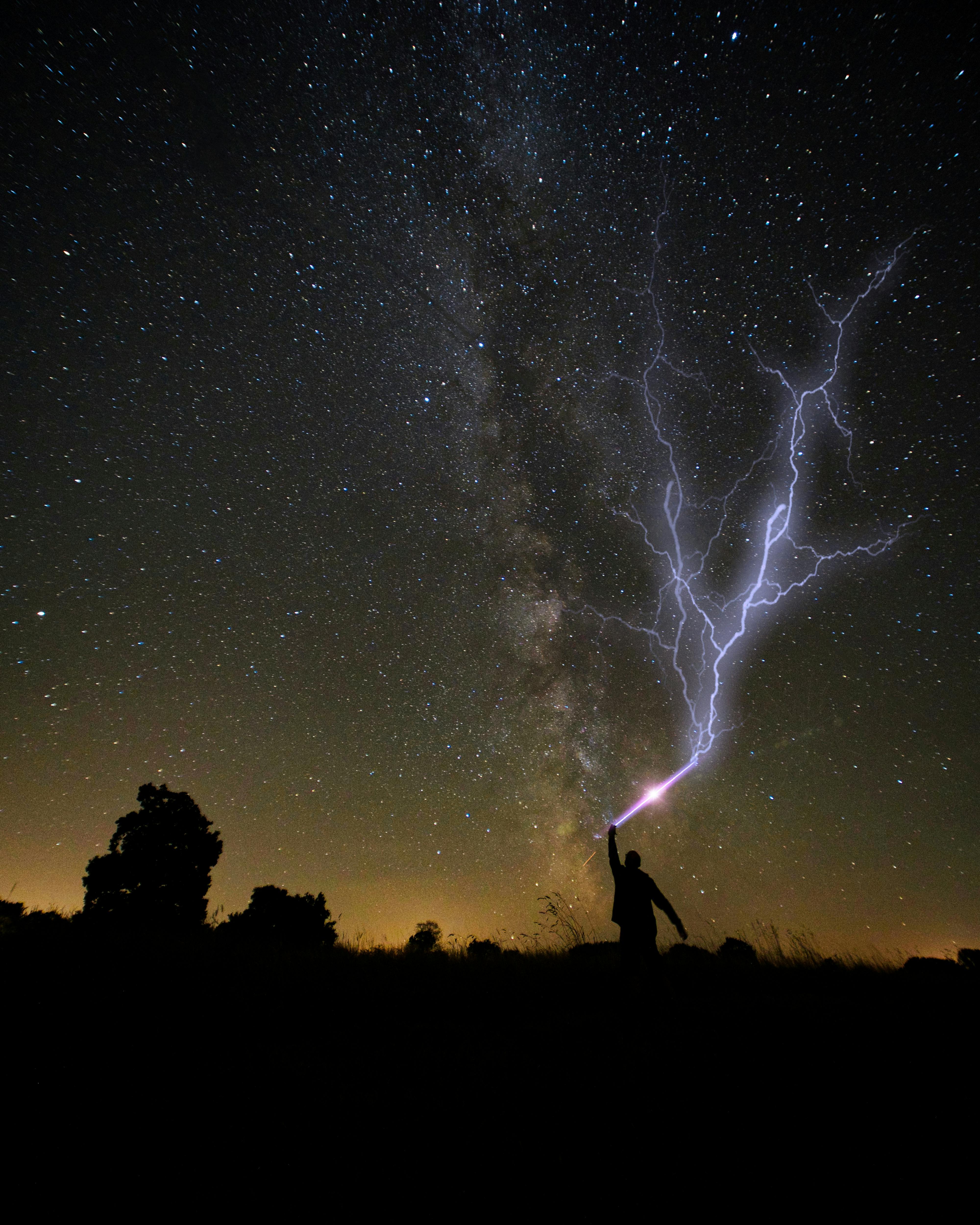 Silhouette of a person with lightning under a starry night sky, creating a dramatic scene.