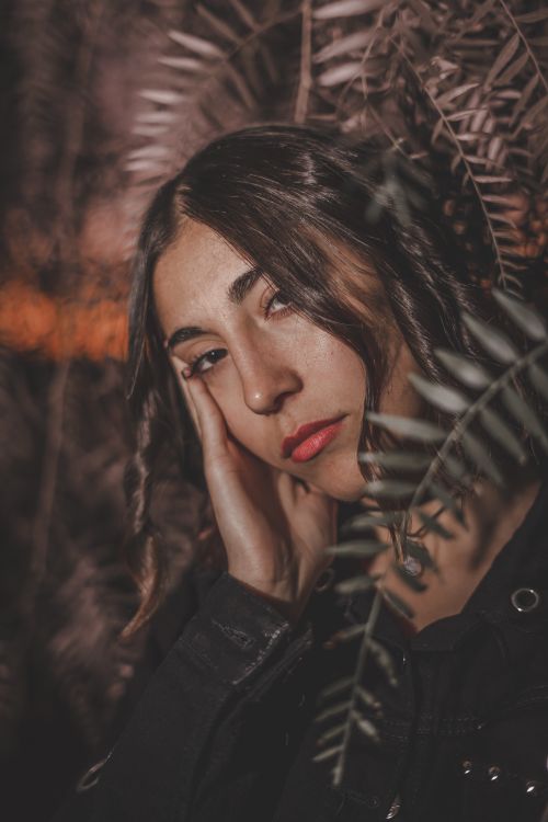 Free A brunette woman poses pensively surrounded by ferns, creating a serene natural portrait. Stock Photo