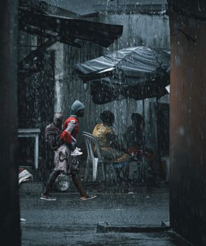 An urban street scene featuring people under umbrellas during heavy rain.