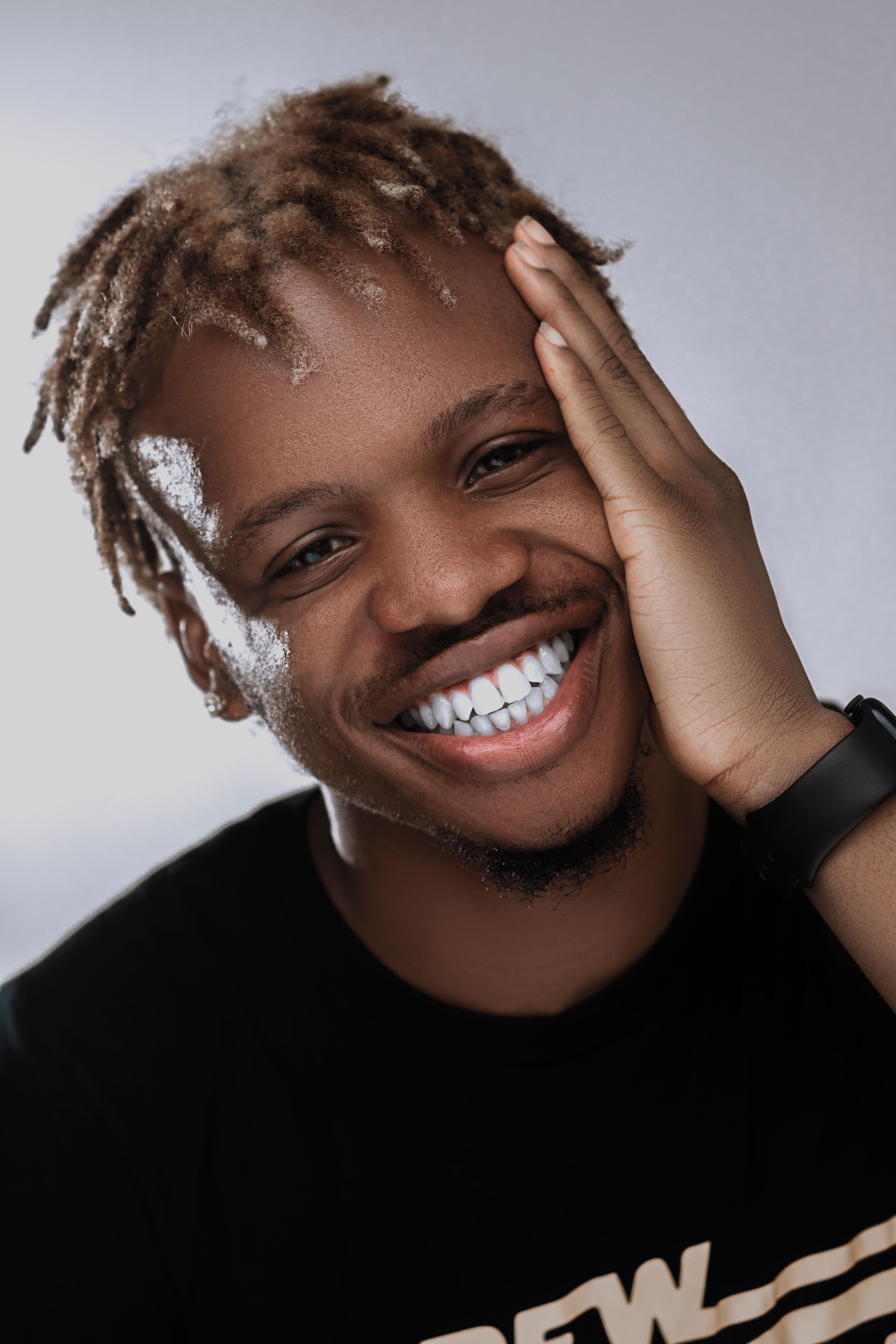 Portrait of a smiling man with dyed dreadlocks in a relaxed pose on a gray background.