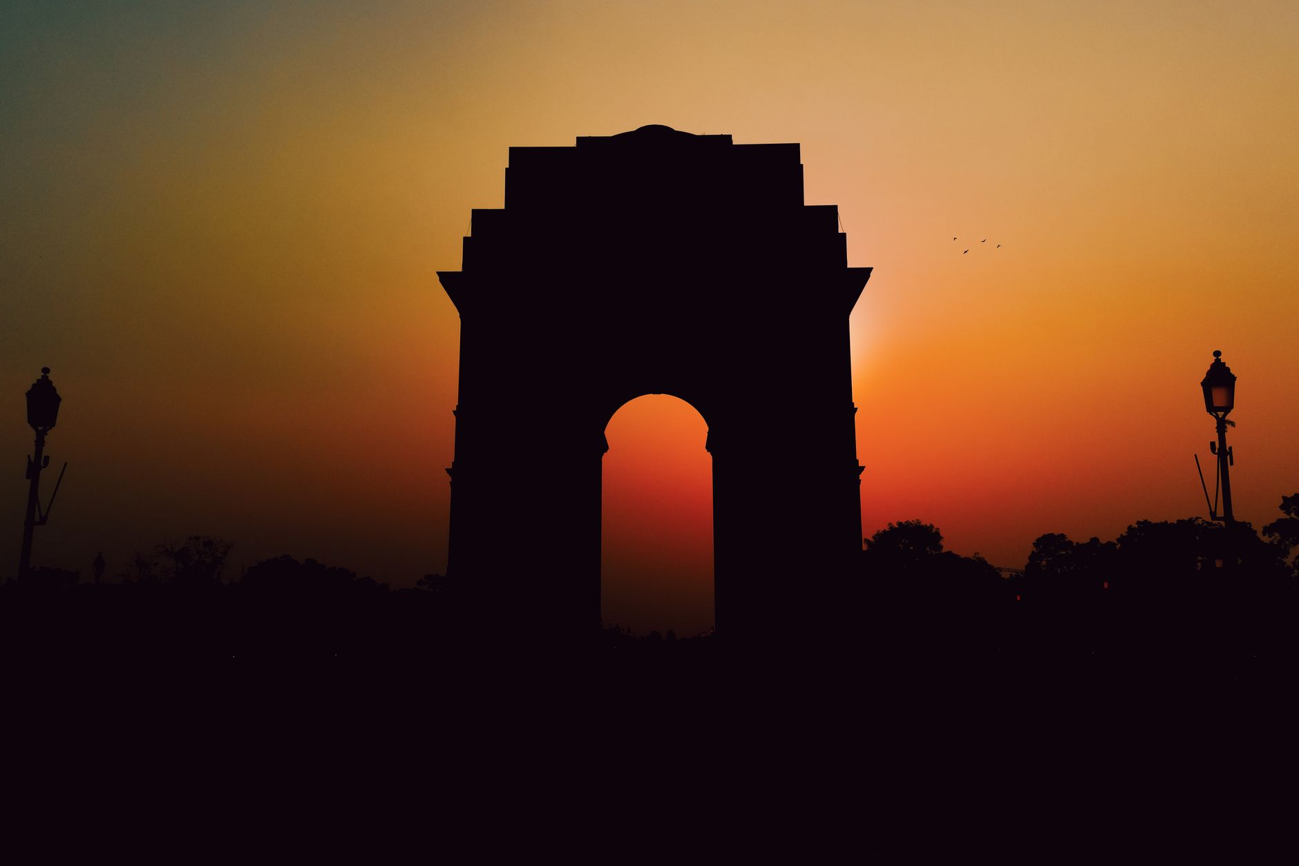 नई दिल्ली के इंडिया गेट के सामने सुबह की हल्की धूप में गुजरते लोग और भारतीय ध्वज