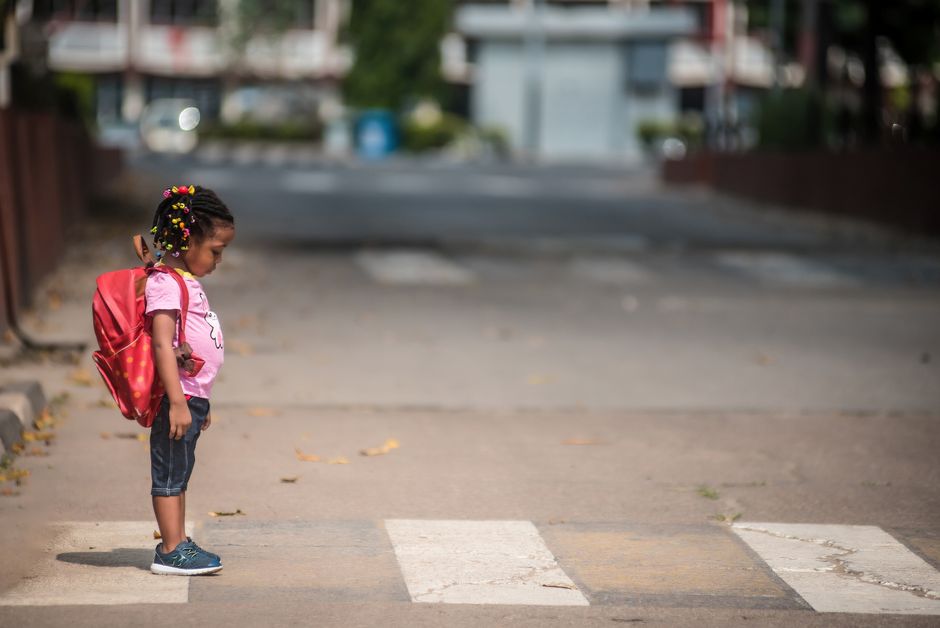 A young child with a backpack standing on a zebra crossing on an urban street.