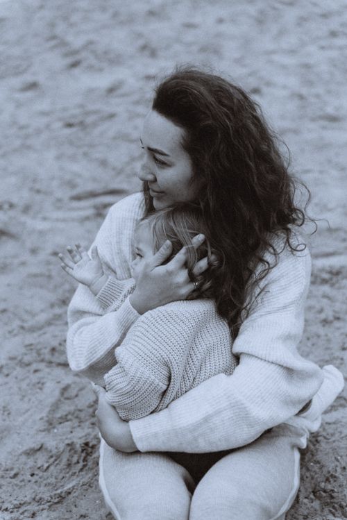 Free A heartwarming moment of a mother hugging her child on a sandy beach in black and white. Stock Photo