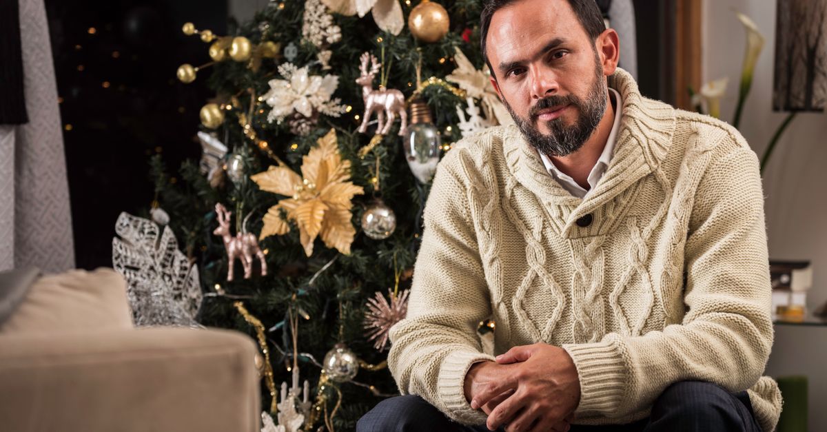 Man in cozy sweater posing by a decorated Christmas tree indoors, creating a festive atmosphere.
