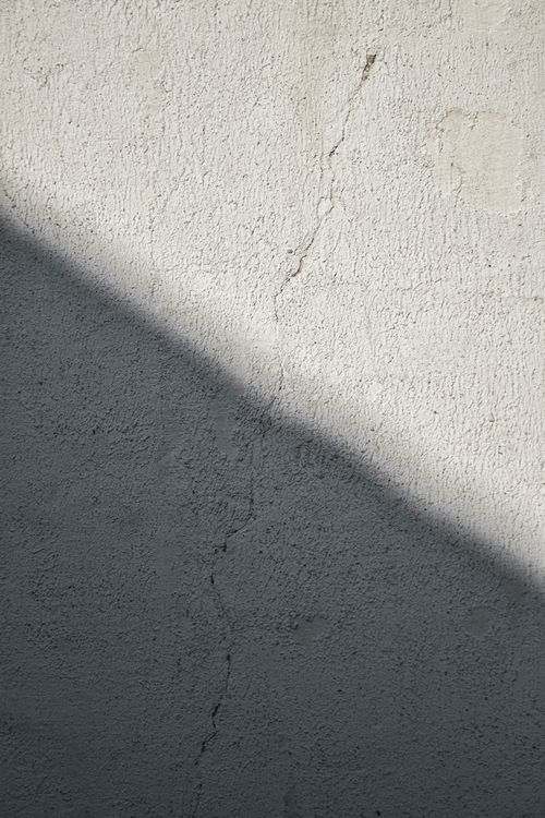 Free A dramatic sunlit shadow casts over a textured concrete wall in a vertical shot. Stock Photo