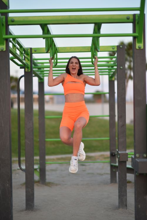Free Woman in neon orange sportswear enjoying an outdoor workout on monkey bars. Stock Photo
