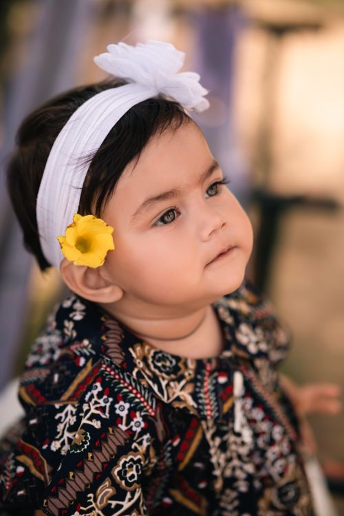 Free Adorable baby with a yellow flower in hairband, wearing colorful attire. Stock Photo