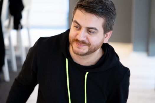 Close-up of a man wearing a black hoodie, looking off-camera with a smile.