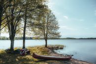 A serene lakeside view featuring a canoe by the shore, trees, and a bench.