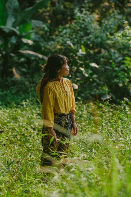 Woman standing in a vibrant green forest, embracing nature's tranquility.