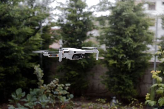 Close-up of a white drone flying outdoors with green foliage in the background.