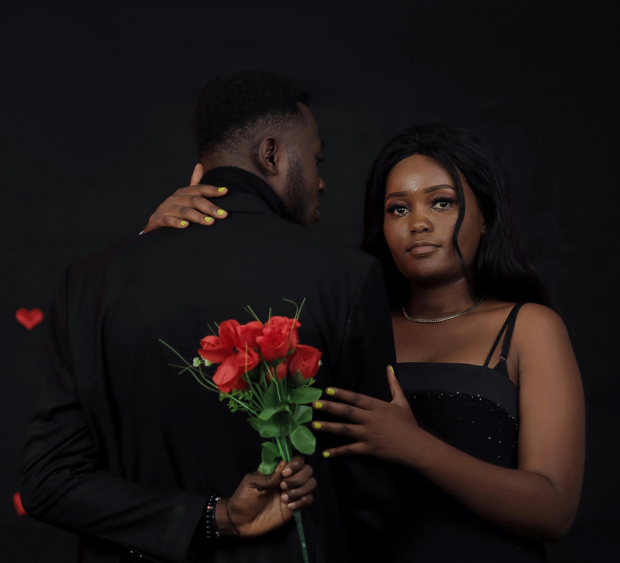 Elegant couple in evening attire with roses, capturing romance in a studio setting.