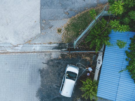 Top-down drone shot of a person washing a car in Ipoh, amidst urban and green surroundings.