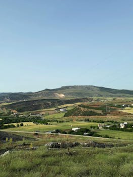 Peaceful countryside view with rolling hills and clear sky during summer.