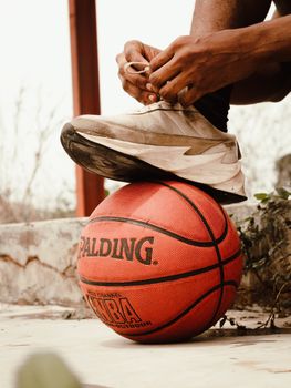 A close-up of a man tying his shoe on a basketball, depicting athletic preparation.