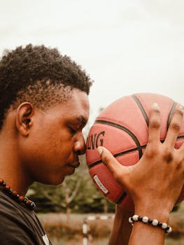Side profile of a young man concentrating on a basketball in an outdoor setting.
