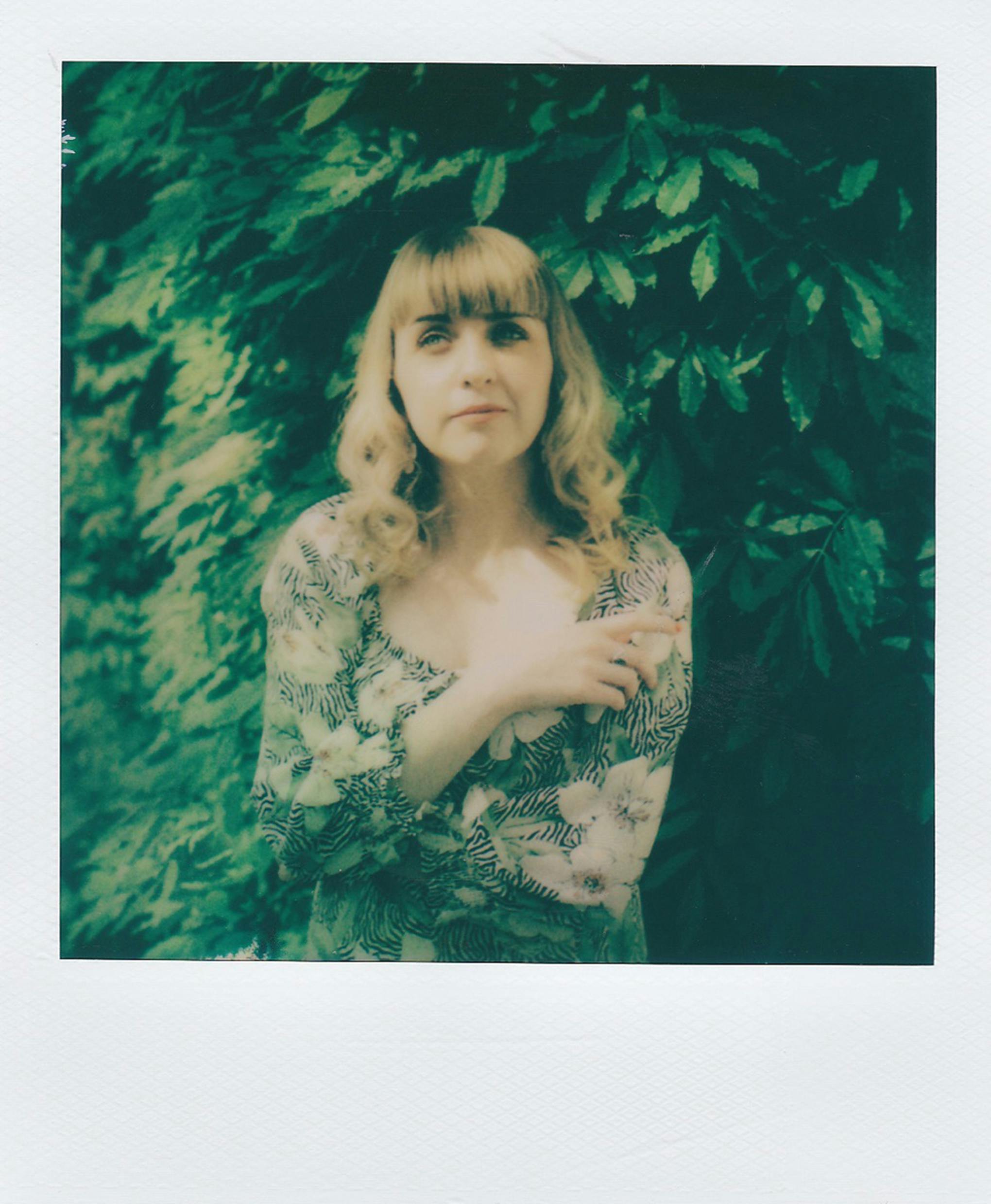 A vintage Polaroid of a woman standing by lush green leaves, evoking a retro vibe.