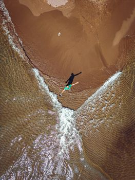 Aerial shot of a person enjoying the waves at a sandy beach intersection.