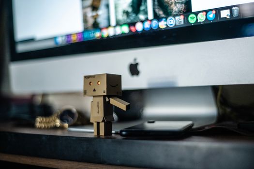 A small cardboard robot toy displayed in front of a computer screen, adding charm to the workspace.