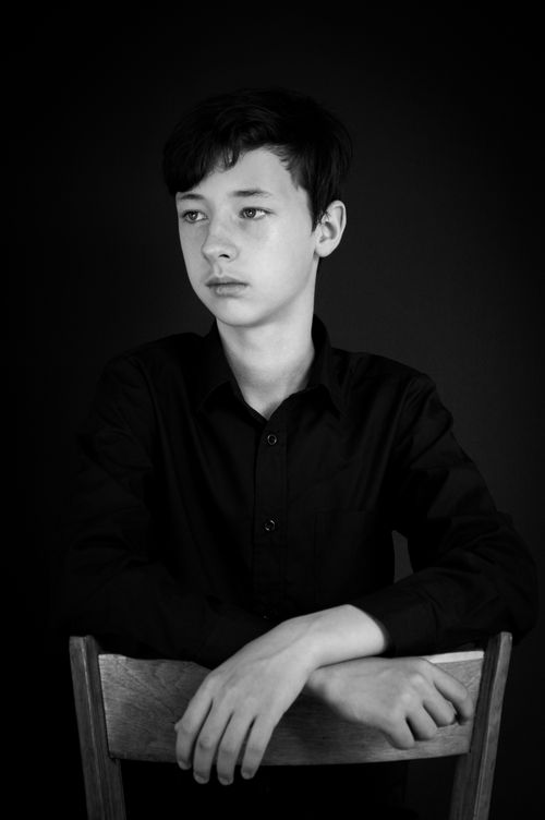 Free Black and white portrait of a young boy in a studio setting, sitting thoughtfully with a serious expression. Stock Photo