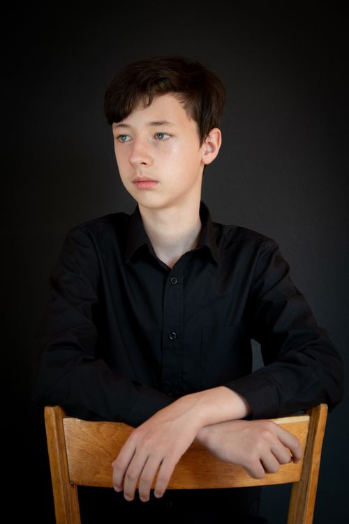 Free Portrait of a teenage boy sitting on a chair with a black background, embodying contemplation. Stock Photo
